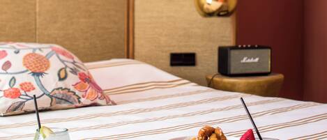 A neatly made bed with a floral pillow, a small speaker, and a tray with food and drinks.
