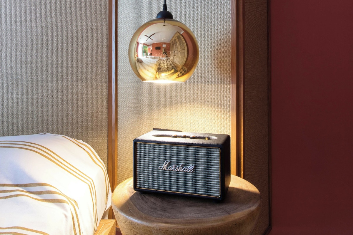 Ein Zimmer mit einem Bett, einem kleinen runden Tisch mit einem Vintage-Radio und einer Pendelleuchte.
