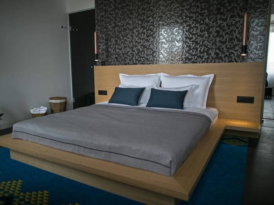 A modern bedroom with a large bed, a dark patterned wall, and a blue rug.