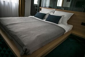 A modern hotel room with a wooden bed frame, grey bedding, and a view of the city through the window. - Rooms Lejletul (Split)