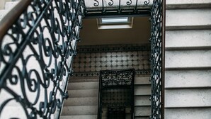 Eine Treppe mit aufwendiger schwarzer Metallreling und einer gefliesten Wand.