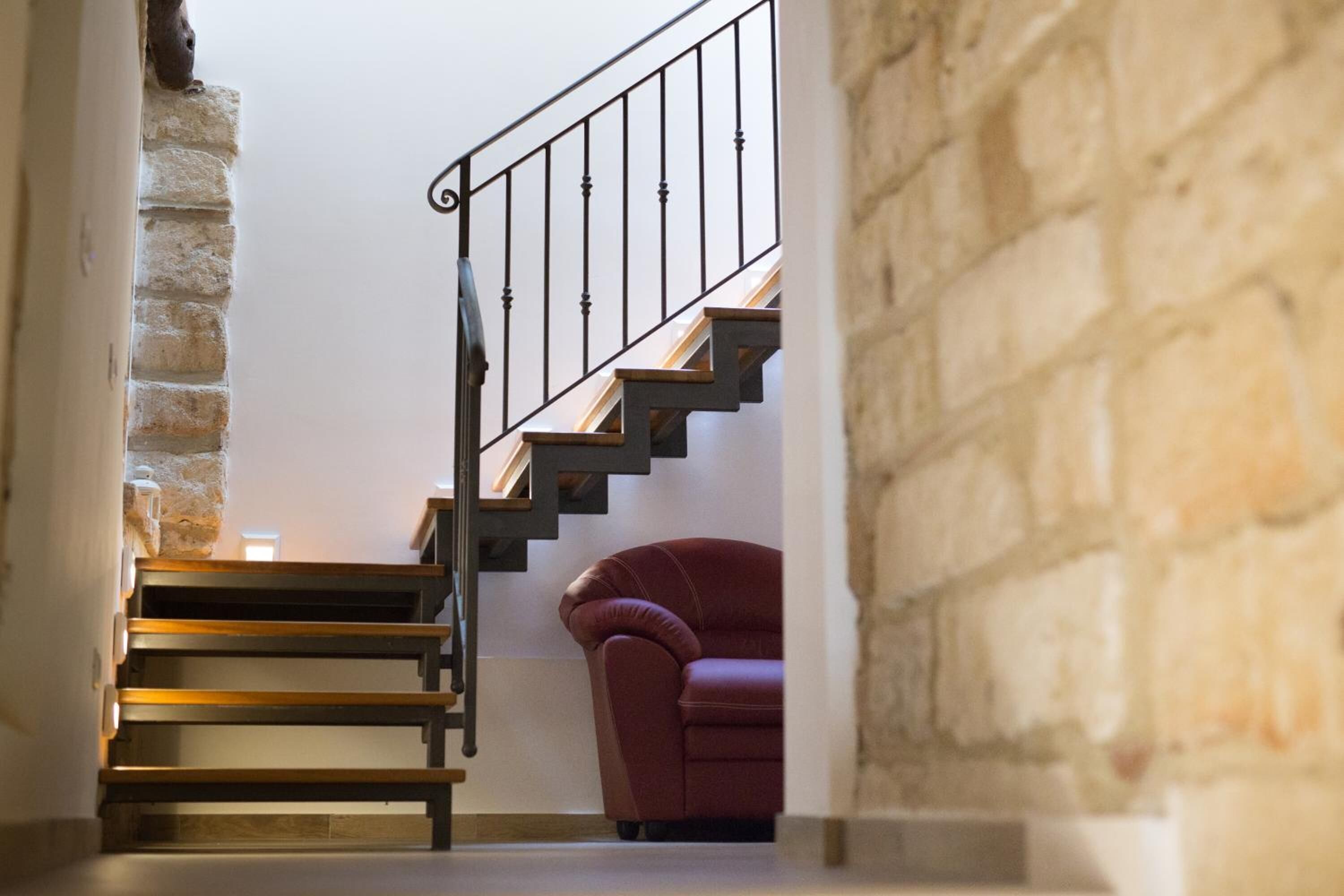 A staircase with wooden steps and a metal railing, leading to a room with a stone wall and a red chair.