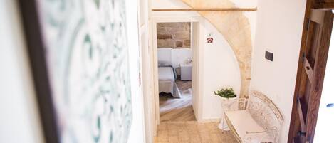 A narrow hallway with a stone archway leading to a bedroom. A white metal bench is placed against the wall near the archway.