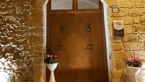 A stone building with a wooden double door, a balcony with metal railings, and two flower pots on either side of the entrance. - Cinisi Vacanze 2.0 (Cinisi)