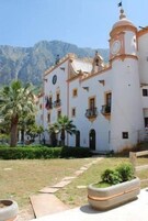 Un edificio con una torre de reloj, varios balcones y un jardín con palmeras.