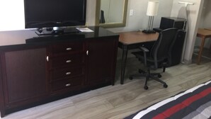 Habitación de hotel con un escritorio de madera, televisor, espejo, lámpara y una silla.