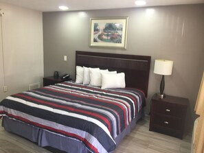 A hotel room with a large bed, a nightstand, a lamp, and a framed picture on the wall.