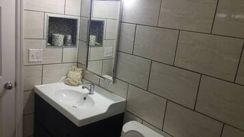 Une salle de bain avec un lavabo blanc, un miroir et des toilettes. Il y a deux distributeurs de serviettes au-dessus du lavabo.
