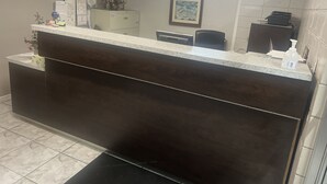 Un mostrador de recepción con acabado de madera oscura, piso de baldosas blancas y un cuadro en la pared.