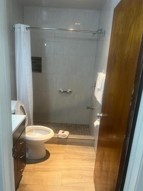 A small bathroom with a shower, toilet, and a wooden door.