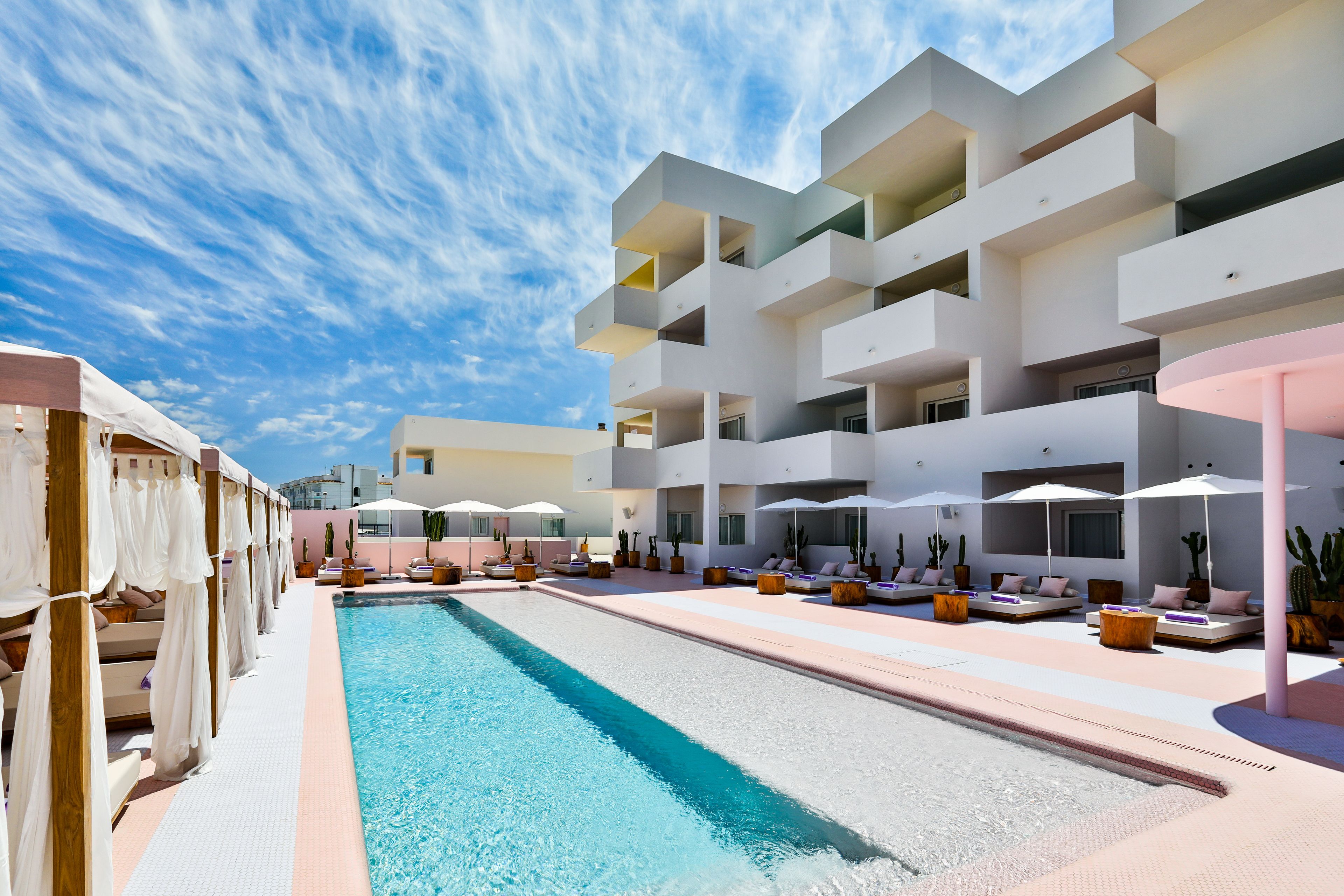 Un hôtel moderne doté d’une piscine, d’un espace extérieur aménagé et offrant une vue sur un ciel d’un bleu éclatant.