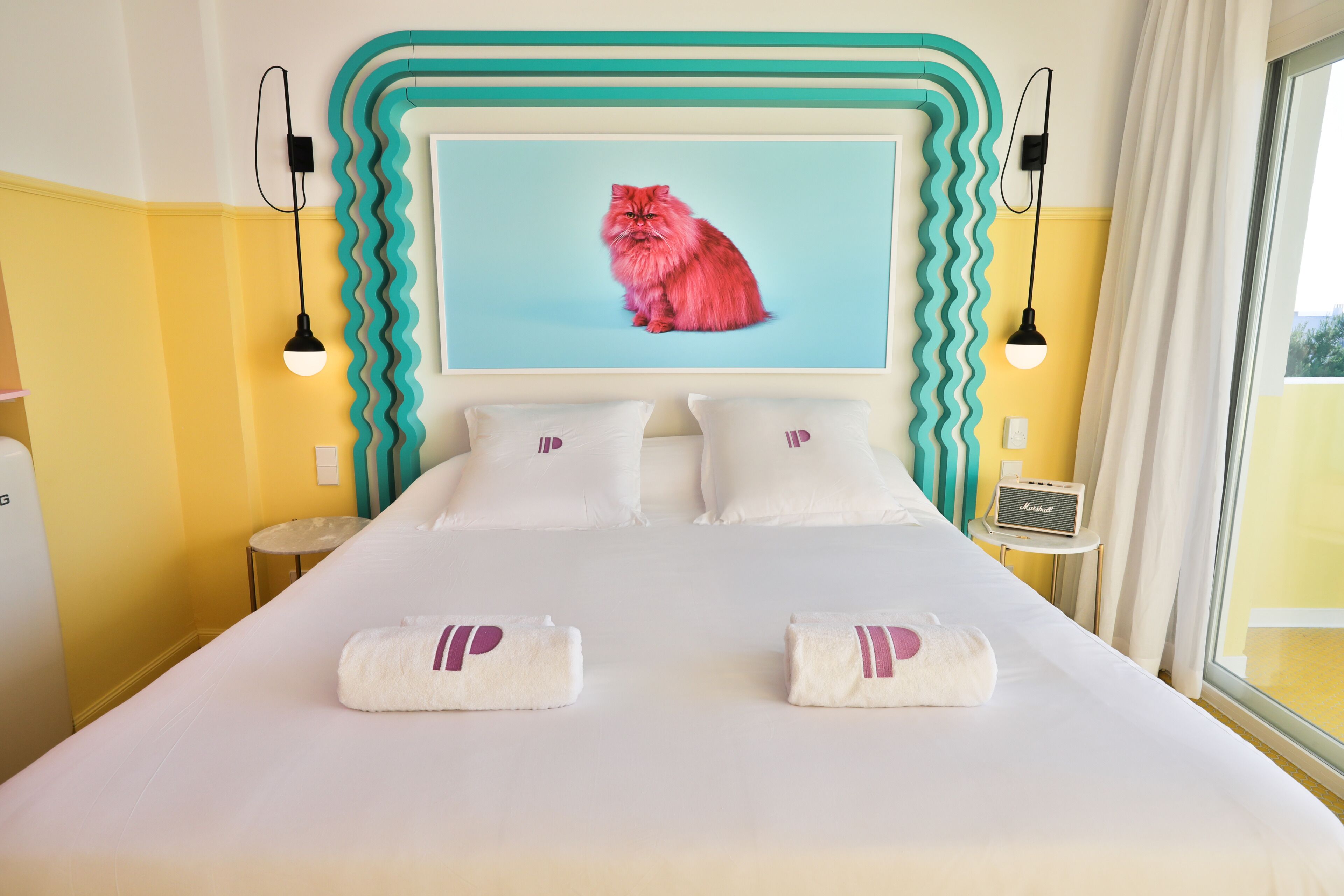A hotel room with a bed, pillows, a wall-mounted picture, a bedside table, and a window.