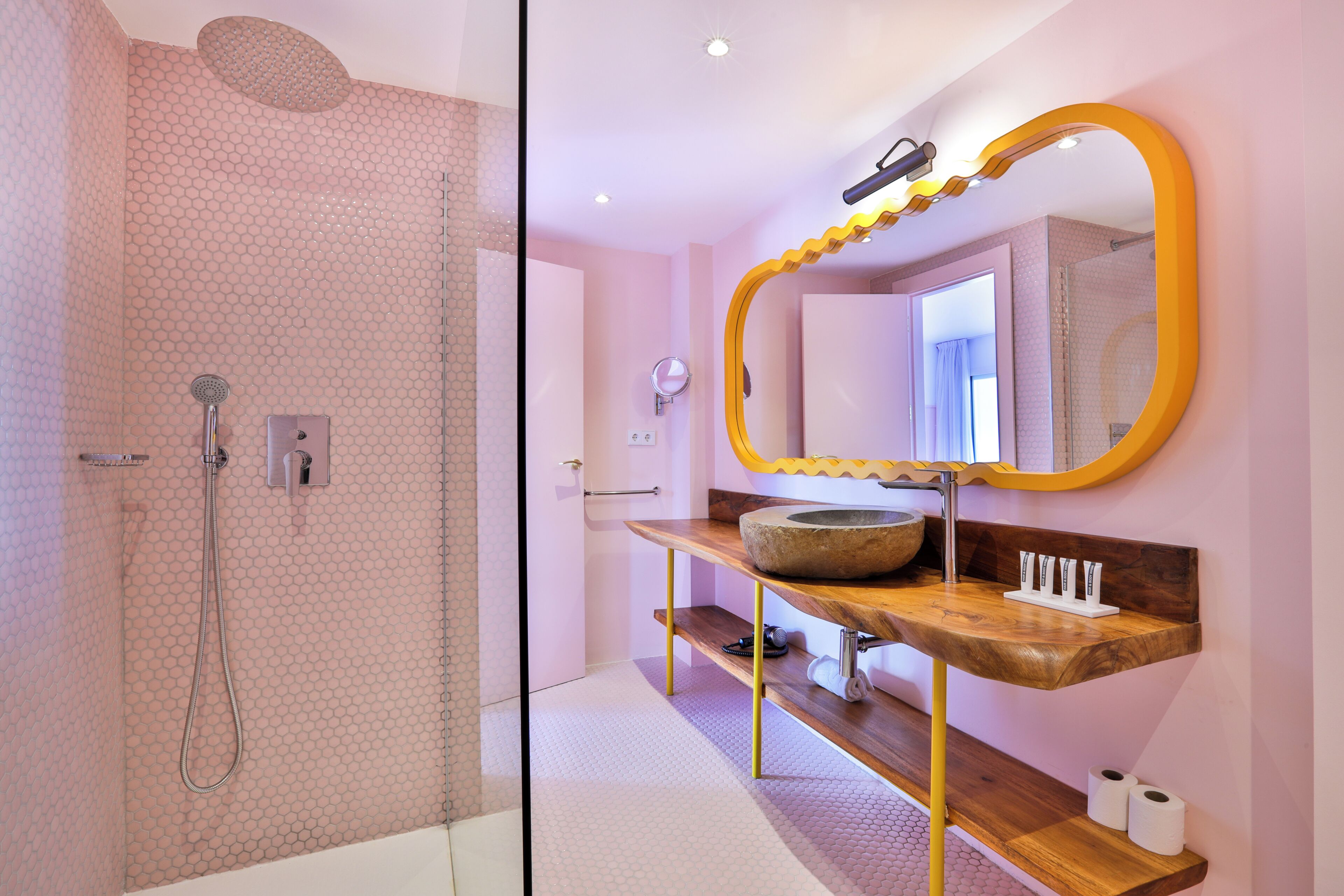 Ein Badezimmer mit Dusche, Waschtisch mit Spiegel und Holzregal.