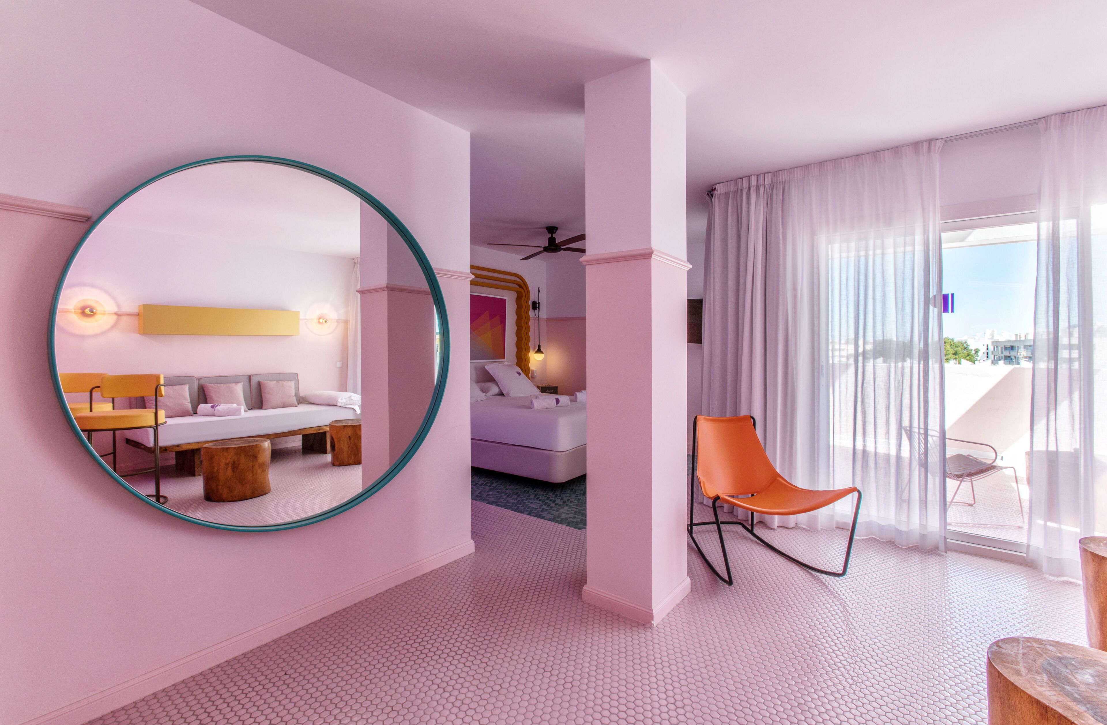 Una habitación de hotel moderna con un espejo redondo, un sofá, una cama y un balcón con vistas.