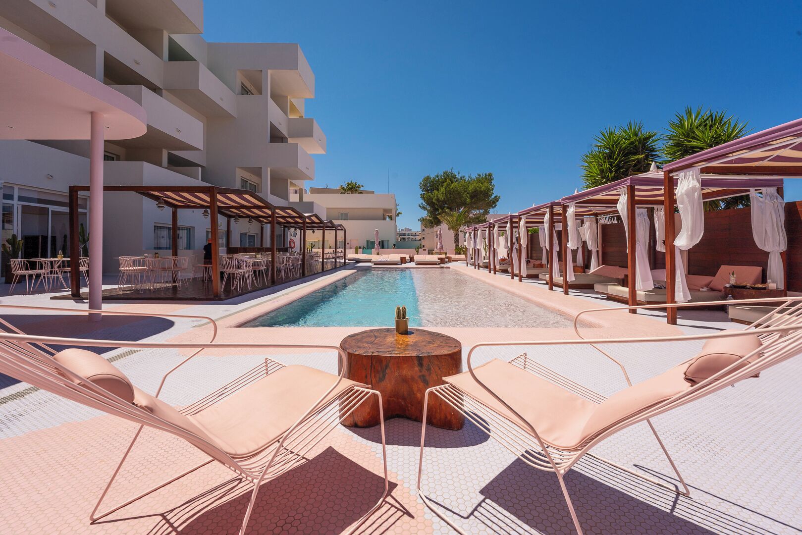 Zona de piscina con sillas de descanso, una chimenea y vistas a un edificio con balcones.