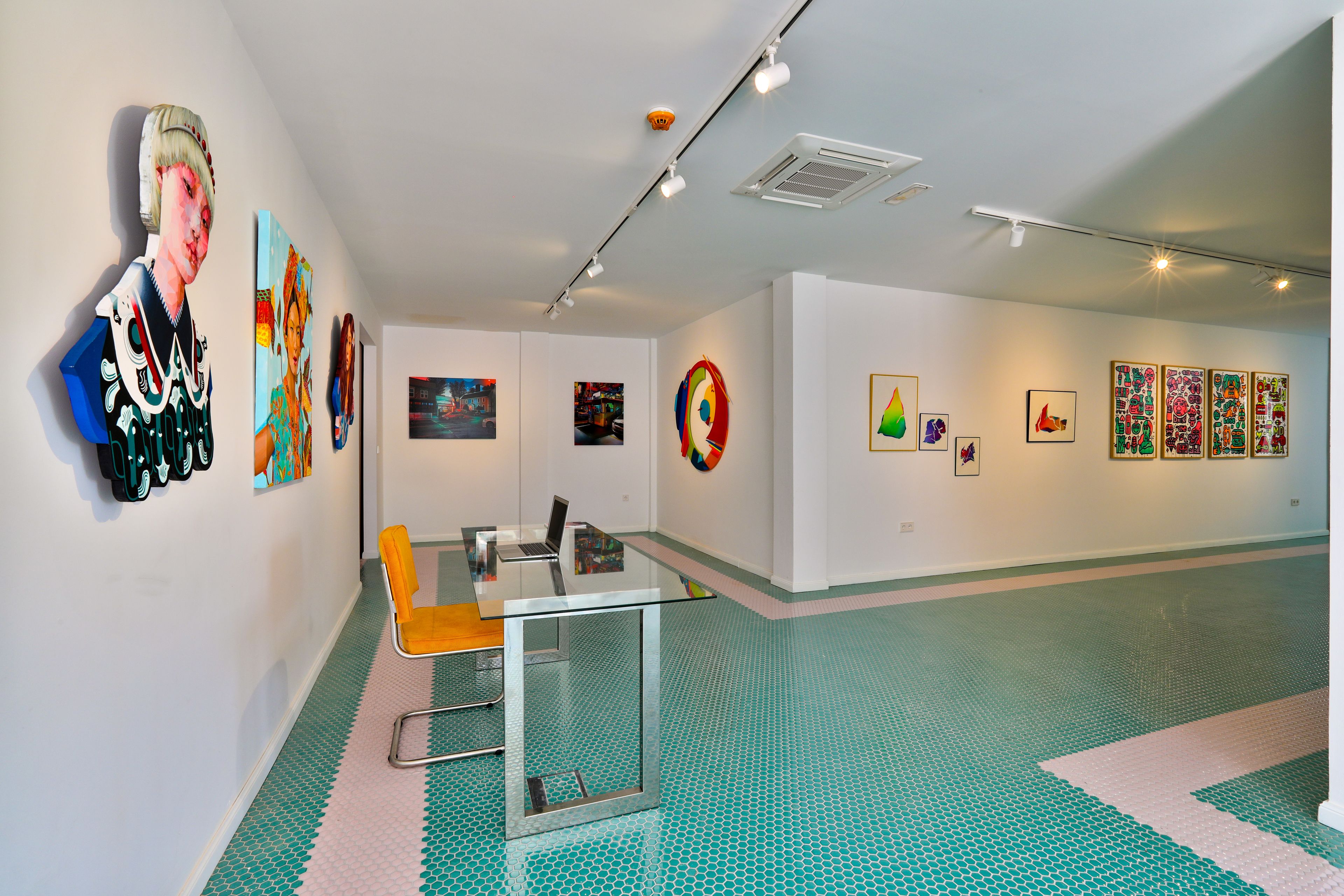 A modern art gallery with a glass table and chairs, a patterned floor, and various artworks on the walls.