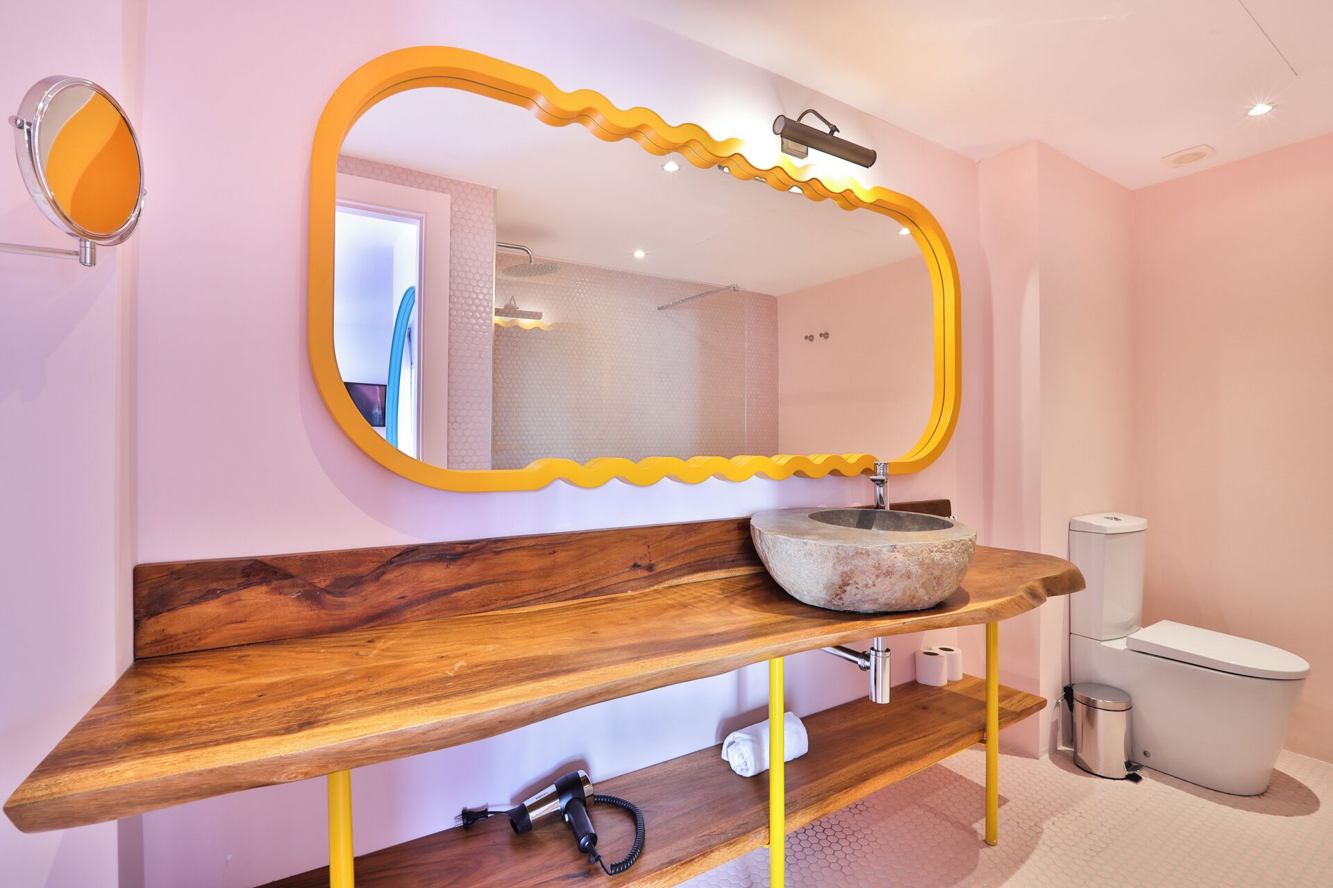 Un baño con tocador de madera, un lavabo redondo, un espejo grande con marco amarillo y un inodoro.