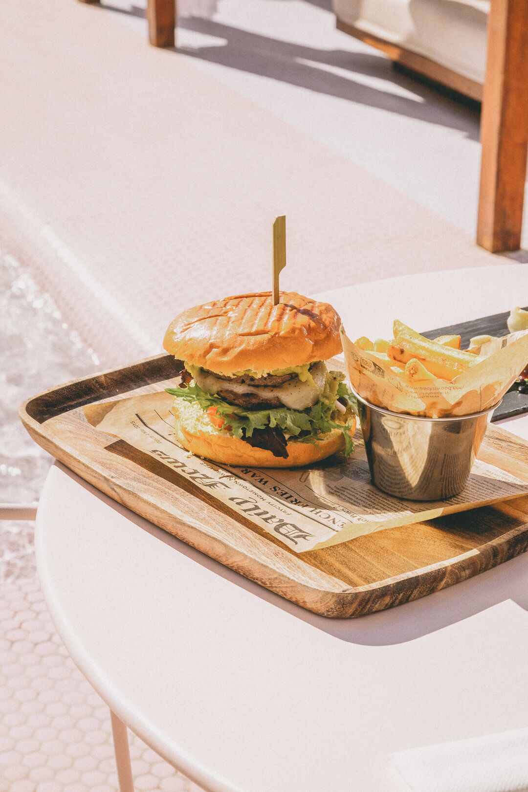 Una hamburguesa con papas fritas sobre una bandeja de madera en una mesa blanca.