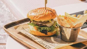 Una hamburguesa con papas fritas sobre una bandeja de madera en una mesa blanca.