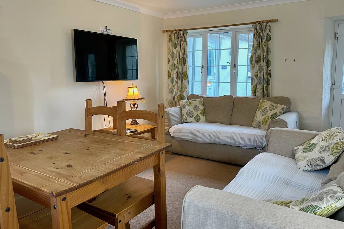 A living room with a wooden dining table, a sofa, and a TV mounted on the wall.
