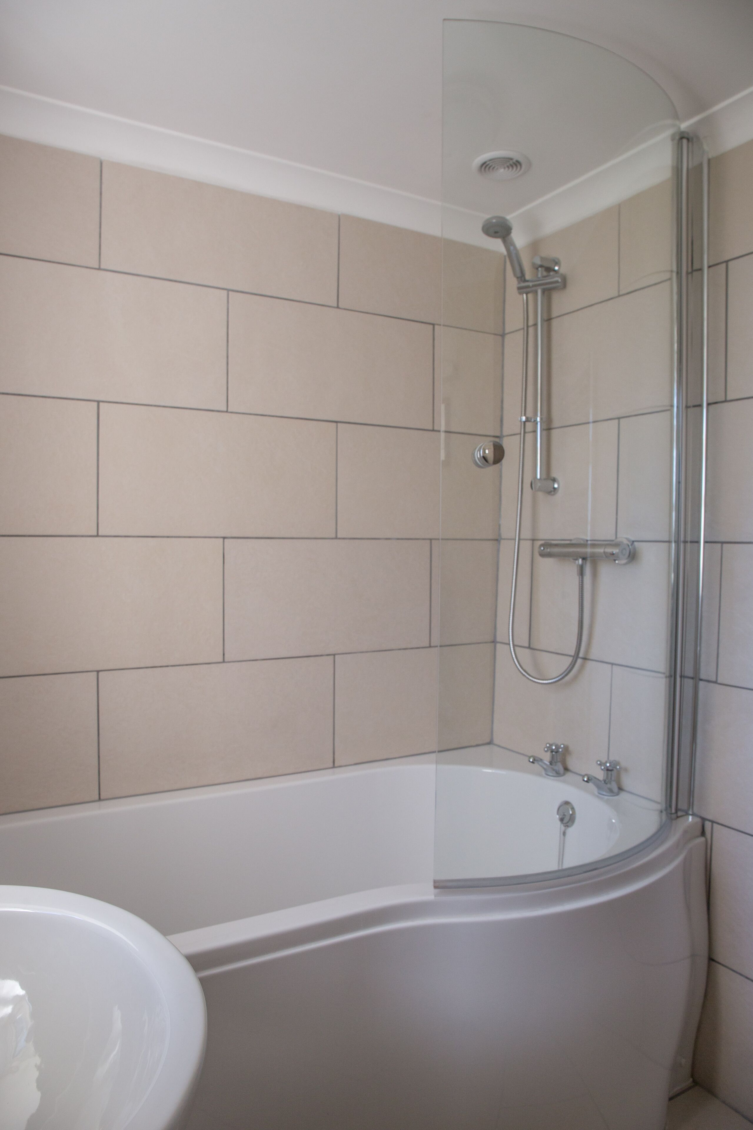 Ein modernes Badezimmer mit einer gläsernen Duschkabine, einer freistehenden Badewanne und beige gefliesten Wänden.