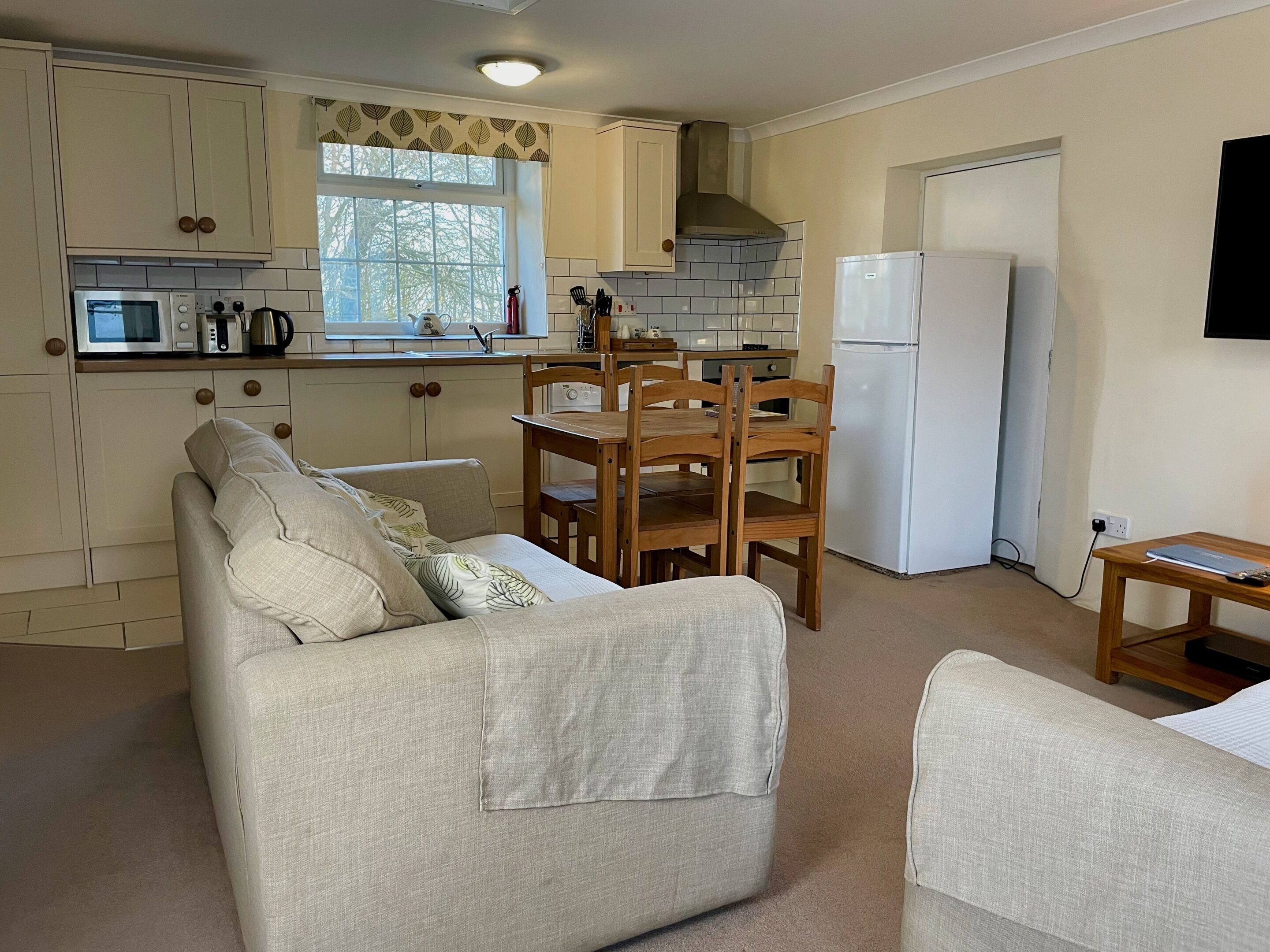 A compact kitchen with white cabinets, a microwave, a stove, and a refrigerator. There is a dining table with chairs and a sofa in the living area.