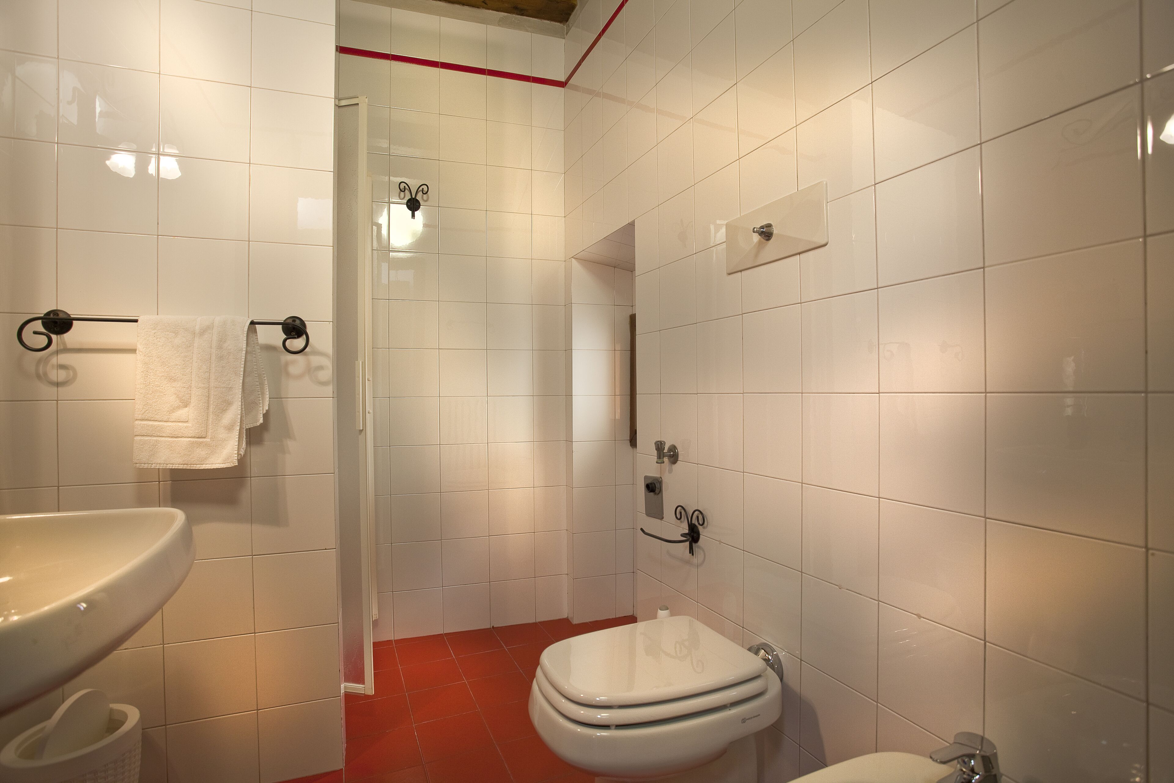 A bathroom with white tiles, a white sink, a toilet, and a shower area.