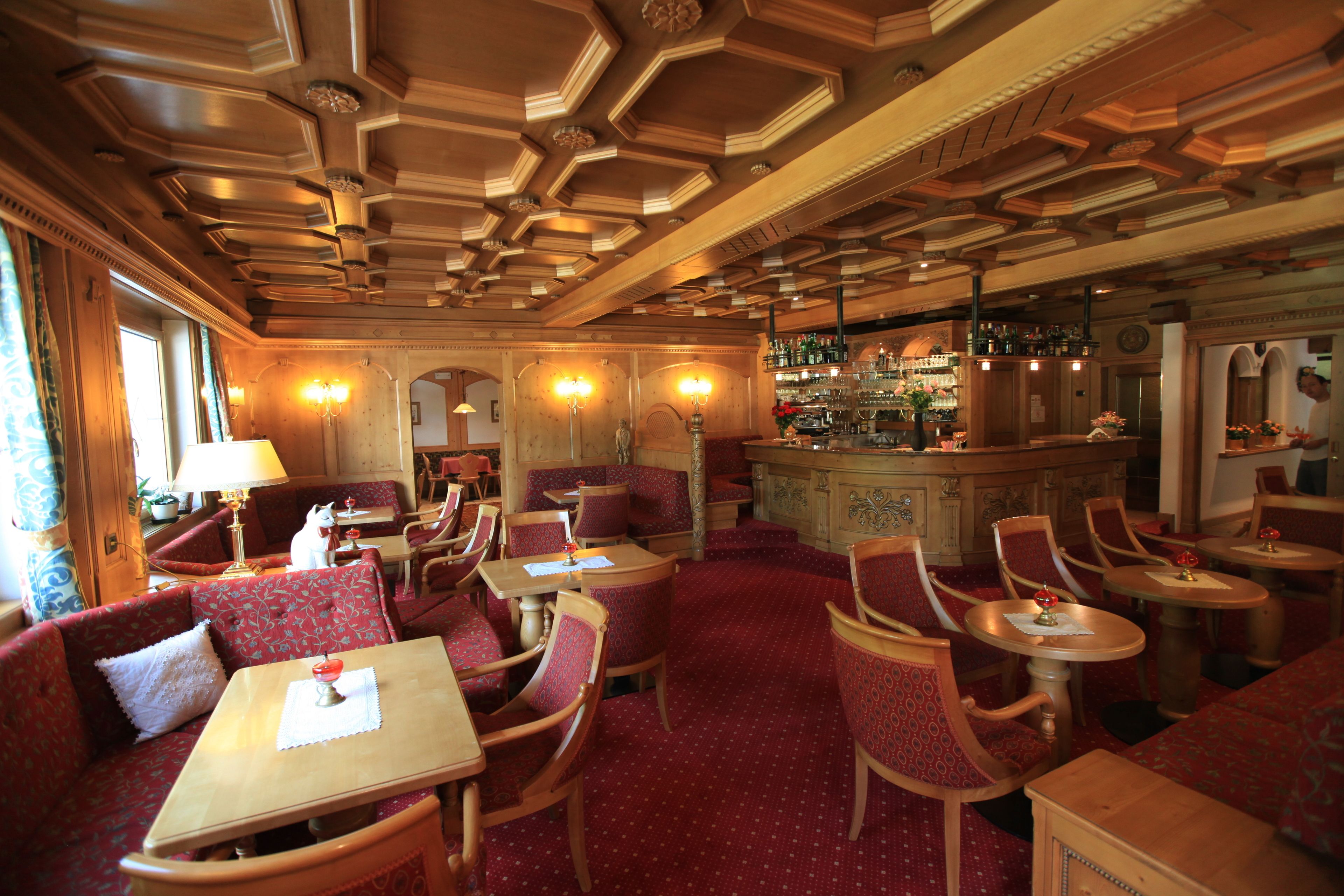 Interior de restaurante con muebles de madera, tapicería roja y una zona de bar.
