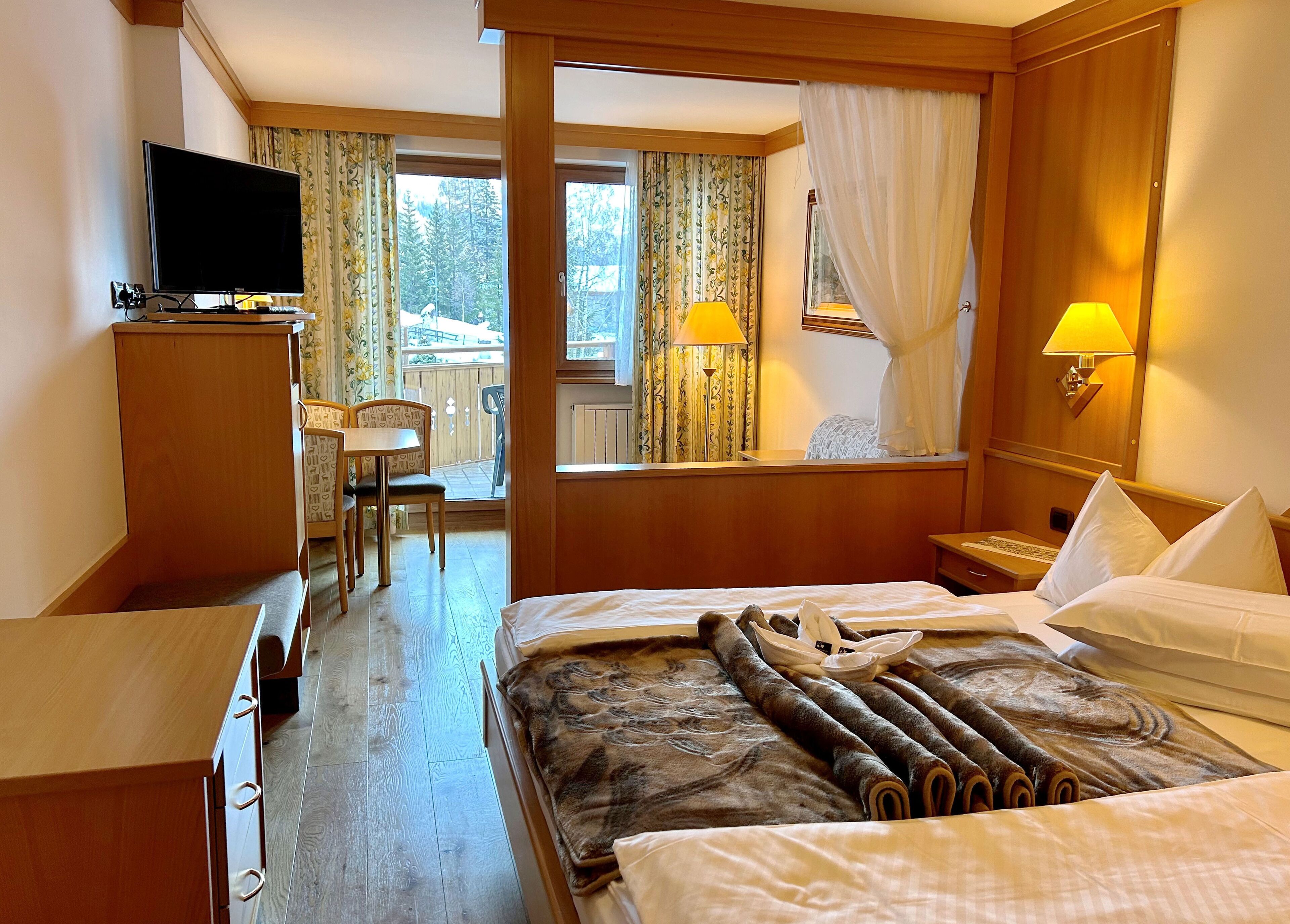 Ein Hotelzimmer mit Bett, Schreibtisch, Fernseher und einem Balkon mit Vorhängen.