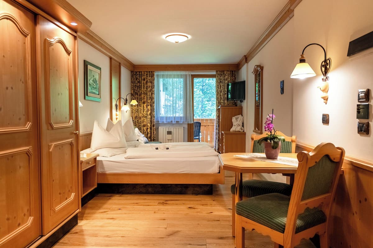 Una habitación de hotel con una cama de madera, una mesa de comedor con sillas, un televisor y una ventana con cortinas.