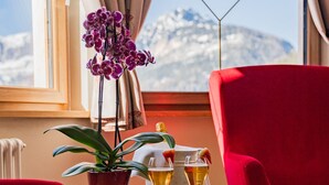 Een kamer met een rode stoel, een tafel met een plant in pot, een wijnglas en een fles champagne.