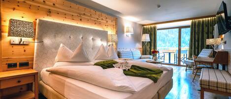 A hotel room with a large bed, a wooden headboard, a desk with a chair, and a balcony with a view of the outdoors.