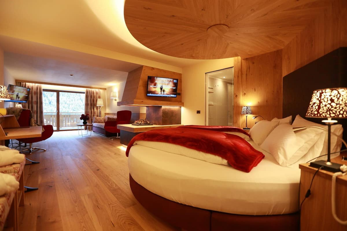 Habitación de hotel moderna con techo curvo, cama grande con una manta roja, televisor en la pared y balcón con vistas.