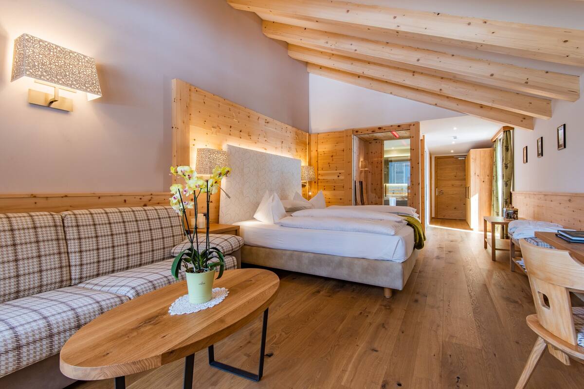 Una habitación acogedora con una cama, un sofá, una mesa de madera con una planta y una lámpara de pared.