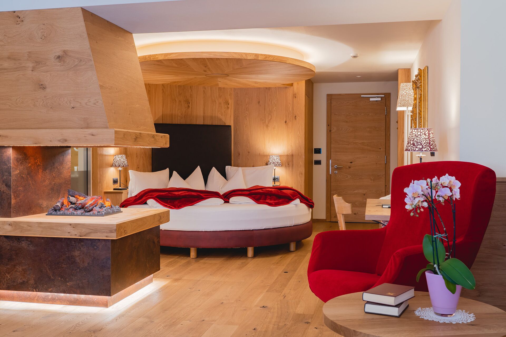 A modern bedroom with a wooden headboard, a red armchair, a bedside table with books, and a small plant.