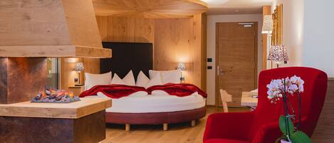 A modern bedroom with a wooden headboard, a red armchair, a bedside table with books, and a small plant.