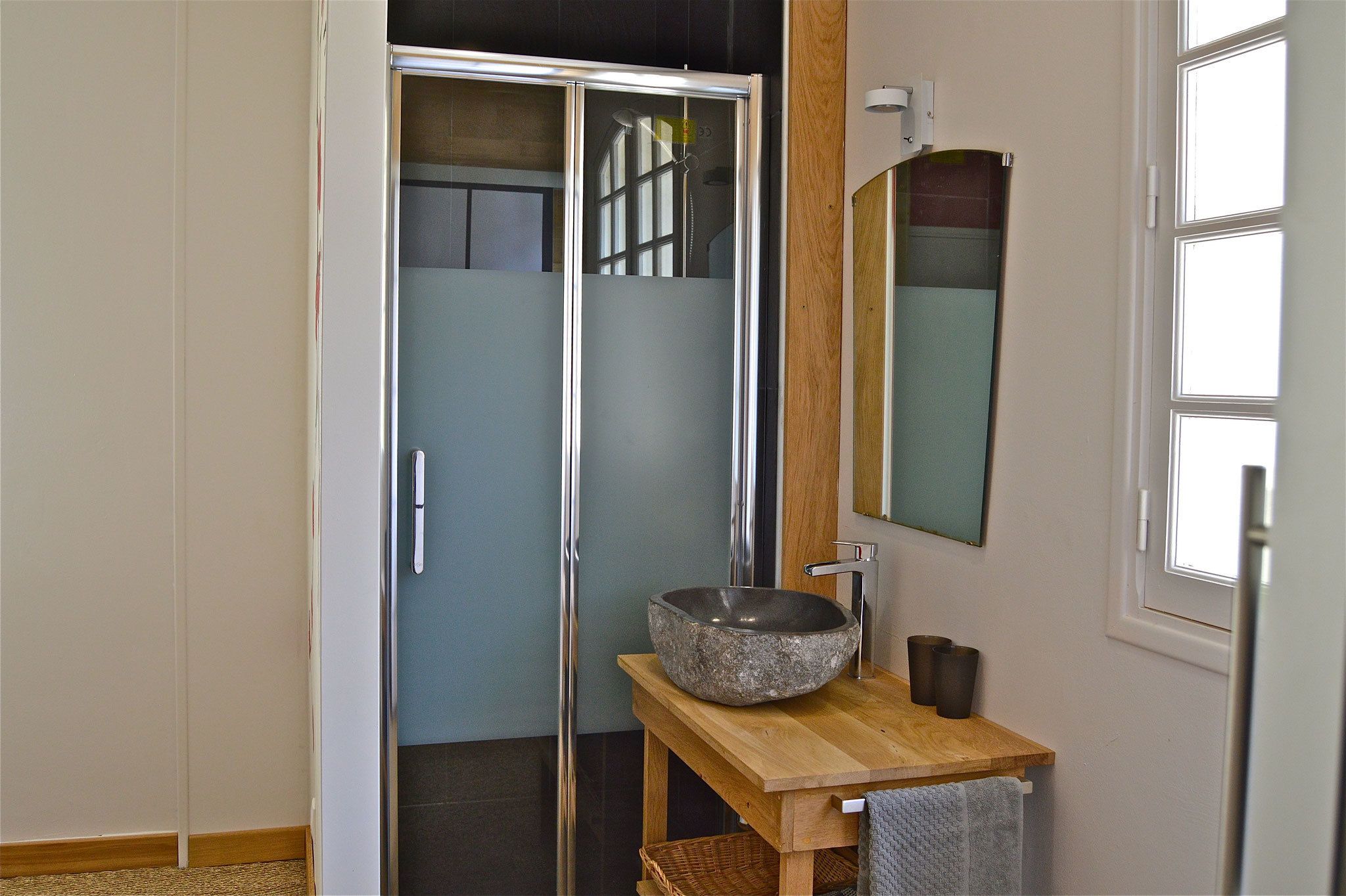 Une salle de bain avec un meuble-lavabo en bois, un lavabo en pierre, un miroir et un espace douche.