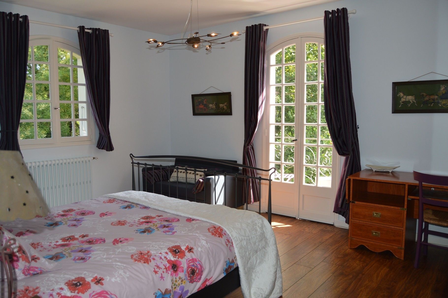 A bedroom with a bed, a dresser, a chair, a radiator, and two windows with curtains.