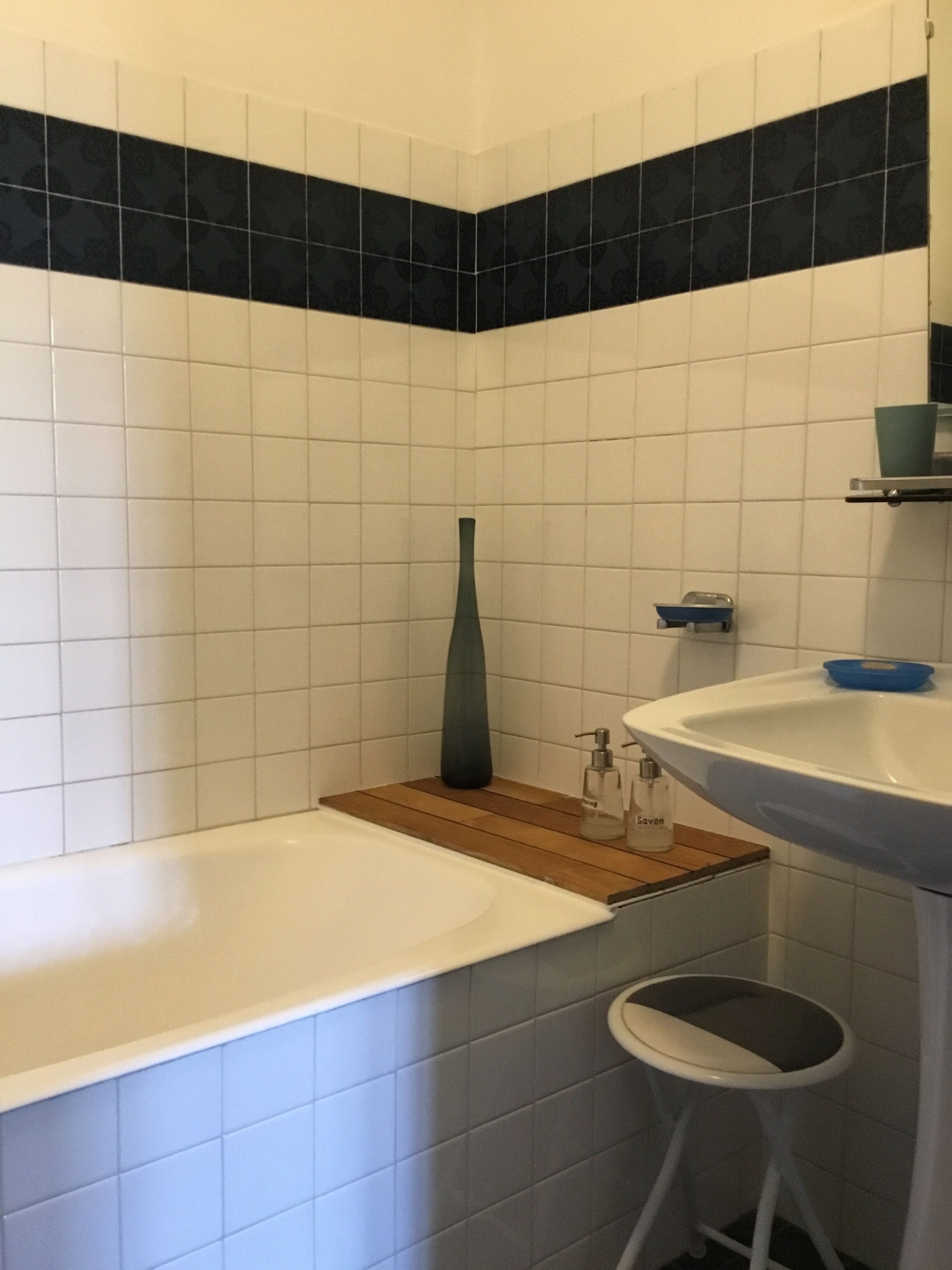 A bathroom with a bathtub, a wooden shelf, a sink, and a toilet.