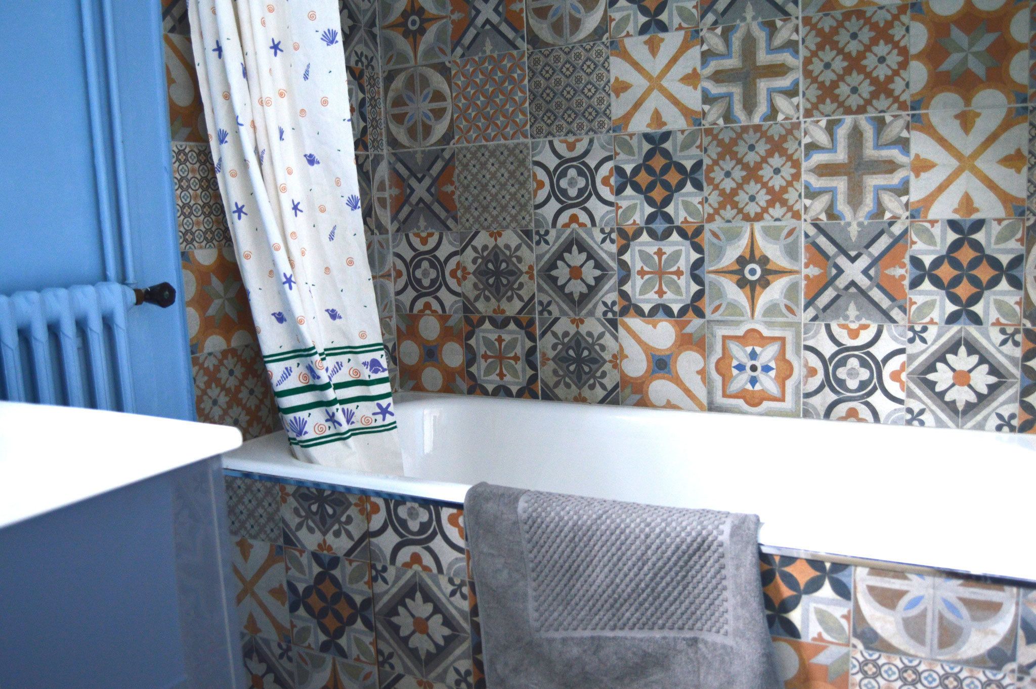 A bathroom with a white bathtub, a towel hanging on the side, and a patterned tile wall.