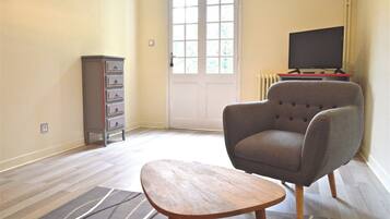 Un salon avec un fauteuil gris, une petite table en bois et un téléviseur posé sur un meuble.