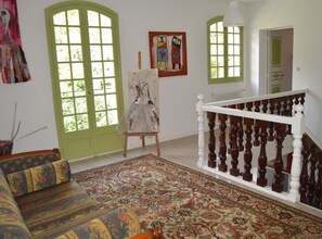 Ein Zimmer mit einem großen floralen Teppich, einer Holztreppe mit weißen Spindeln und zwei Fenstern in grünen Rahmen.