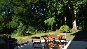 Un patio al aire libre con una mesa y sillas de madera, rodeado de abundante follaje y árboles.