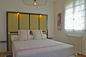A neatly made bed with a headboard, a bedside table, a radiator, and a window with a view of trees. - Maison d'hôtes L'Escalère (Arnaud-Guilhem)