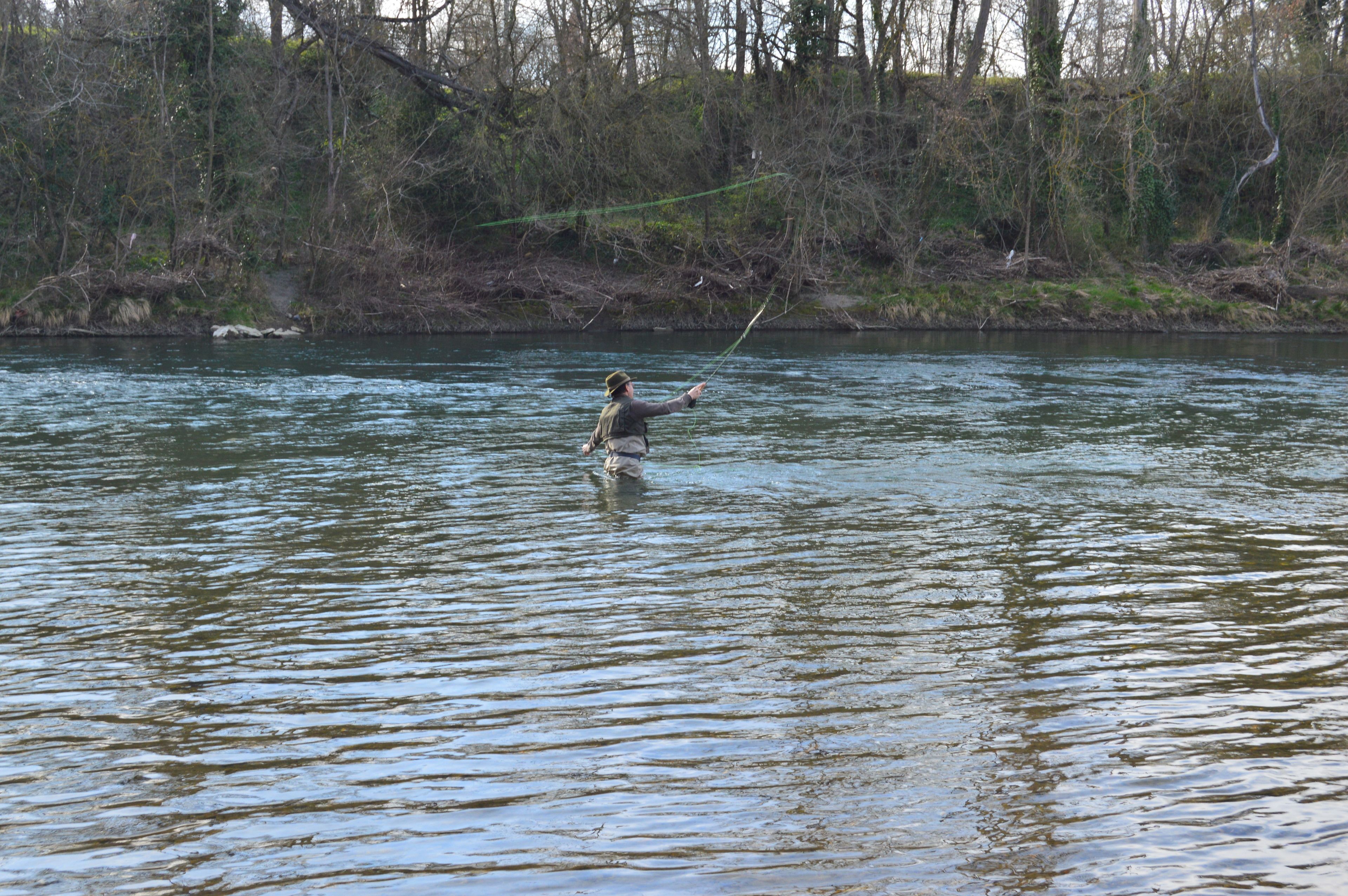 Iemand aan het vissen in een rustige rivier, omgeven door bomen.