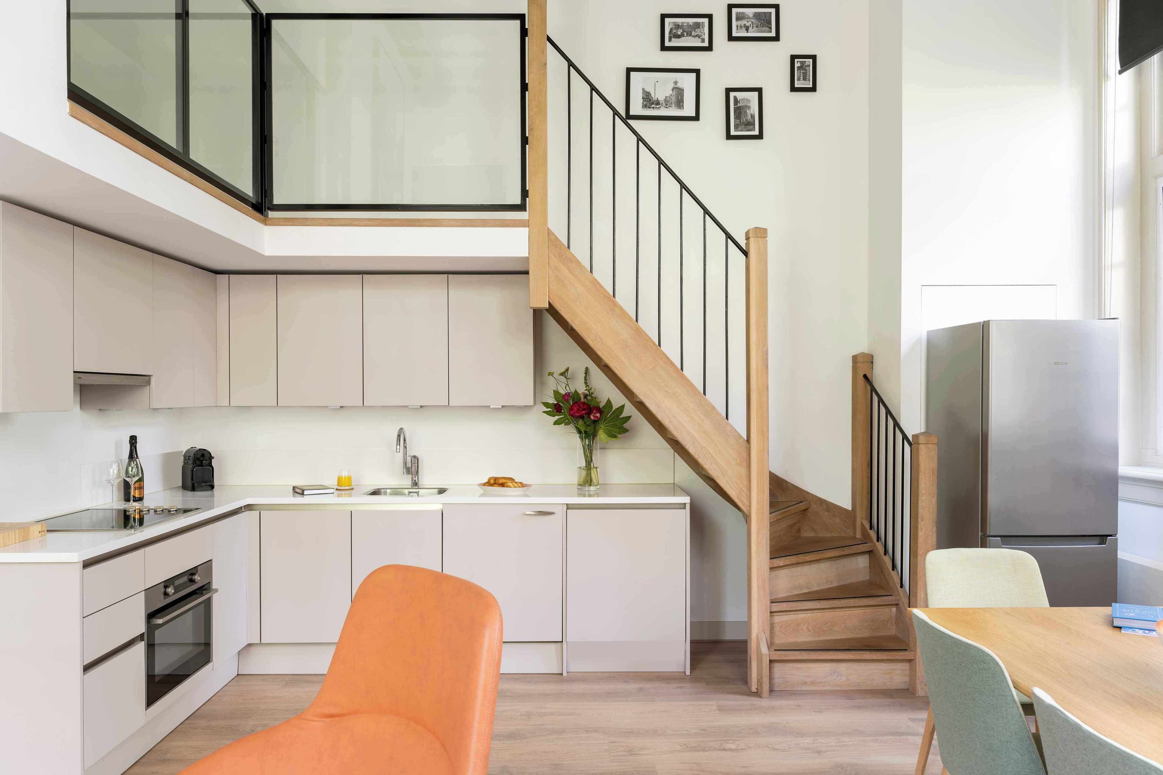 Een moderne keuken met witte kasten, een houten trap en een eethoek met een tafel en stoelen.