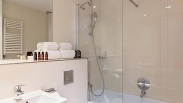 Een moderne badkamer met een douche met glazen wand, een witte wastafel en keurig opgevouwen handdoeken.