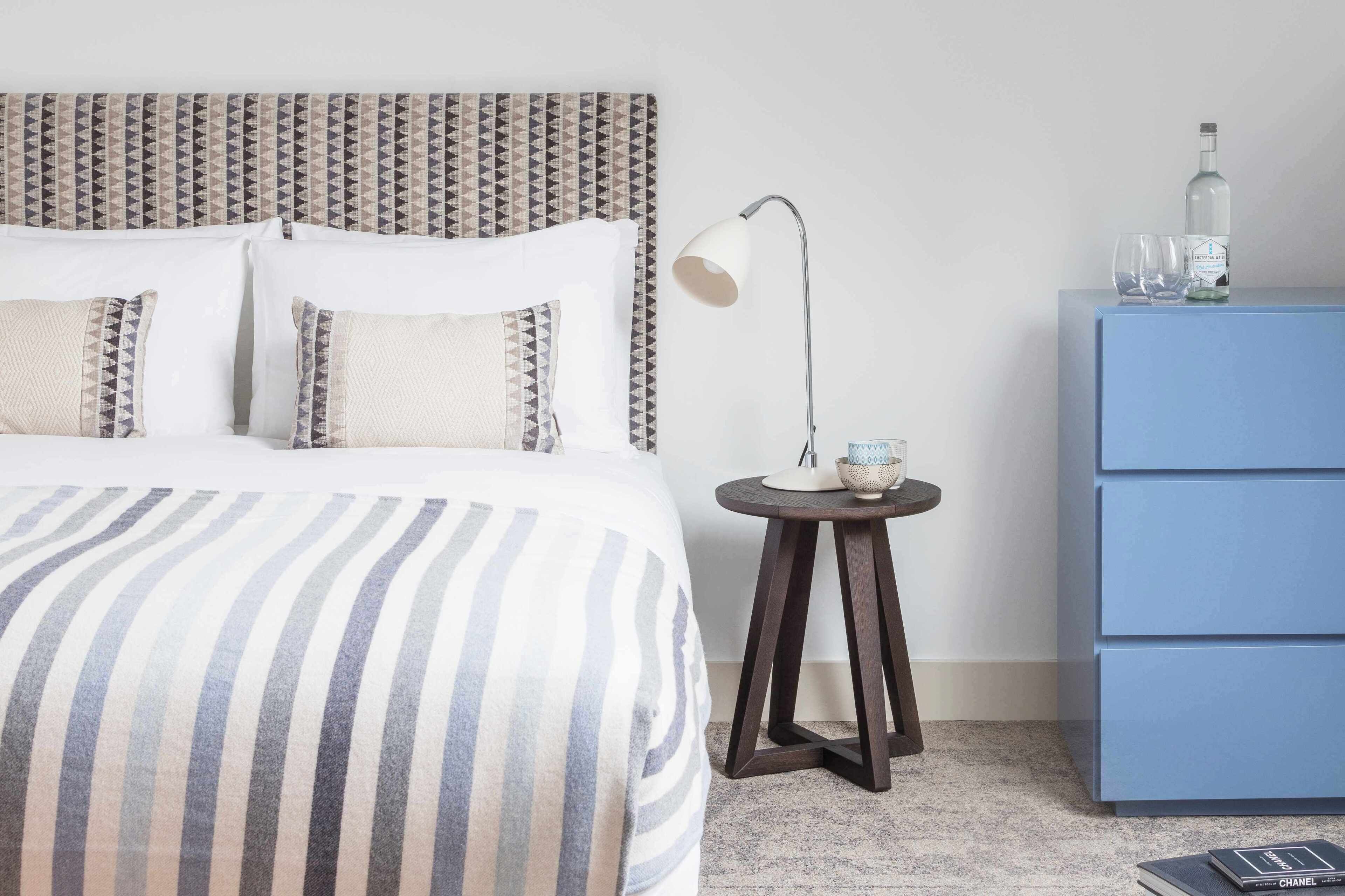 Une chambre d’hôtel bien rangée, avec un lit, une lampe de chevet et une commode bleue.