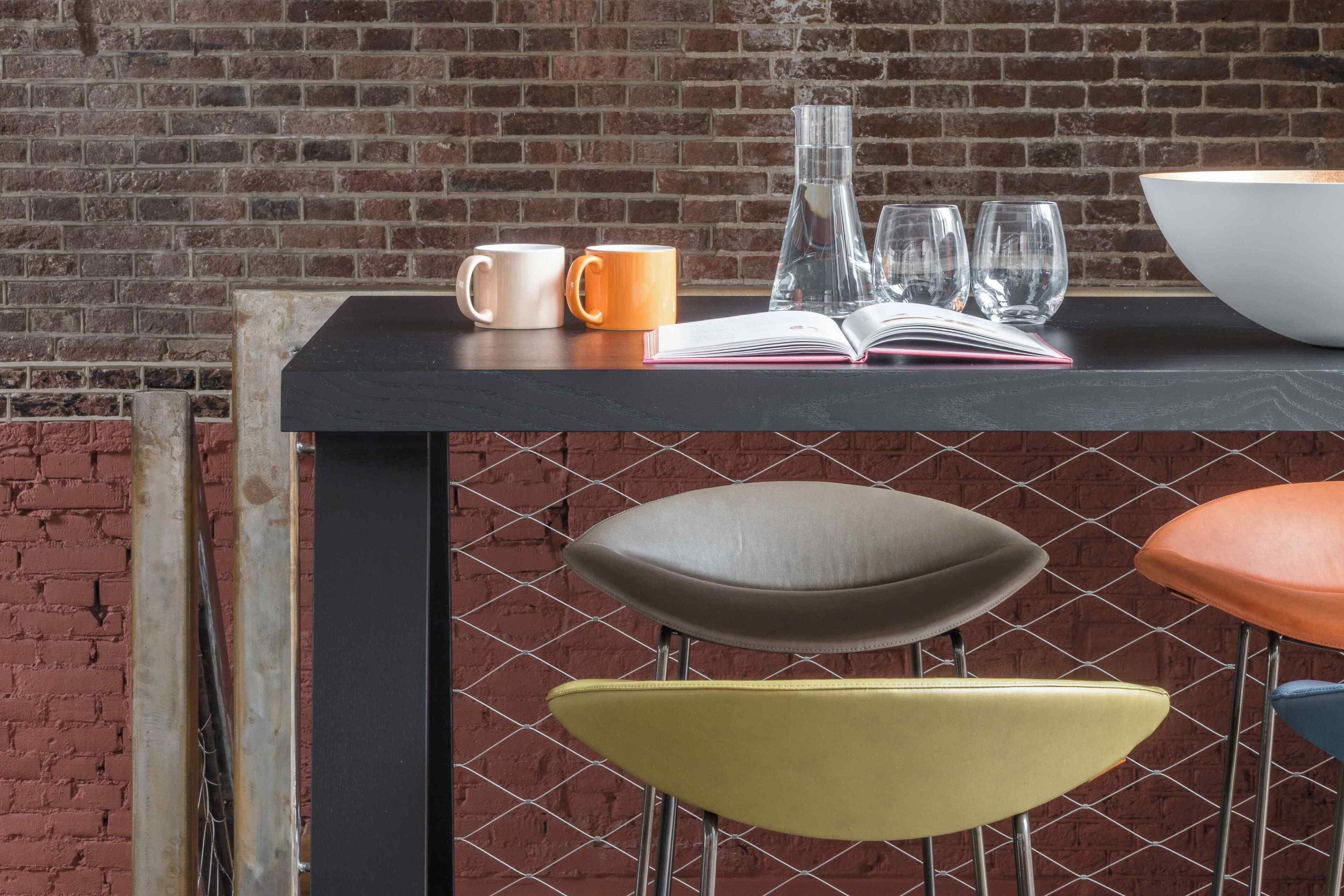 A bar area with stools, a table with a book, a bowl, and two cups.