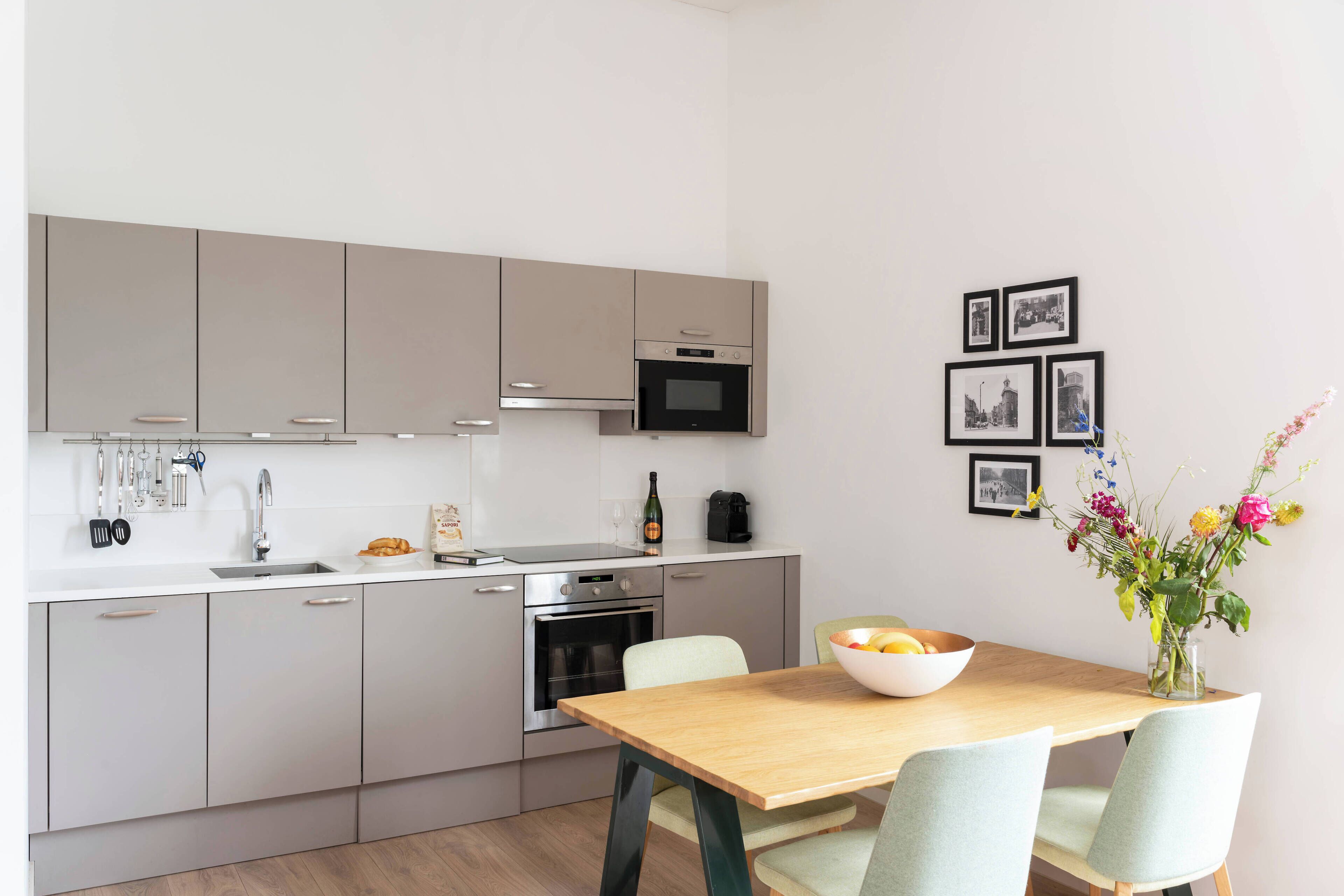 A modern kitchen with stainless steel appliances, a dining table with chairs, and a vase with flowers on the wall.